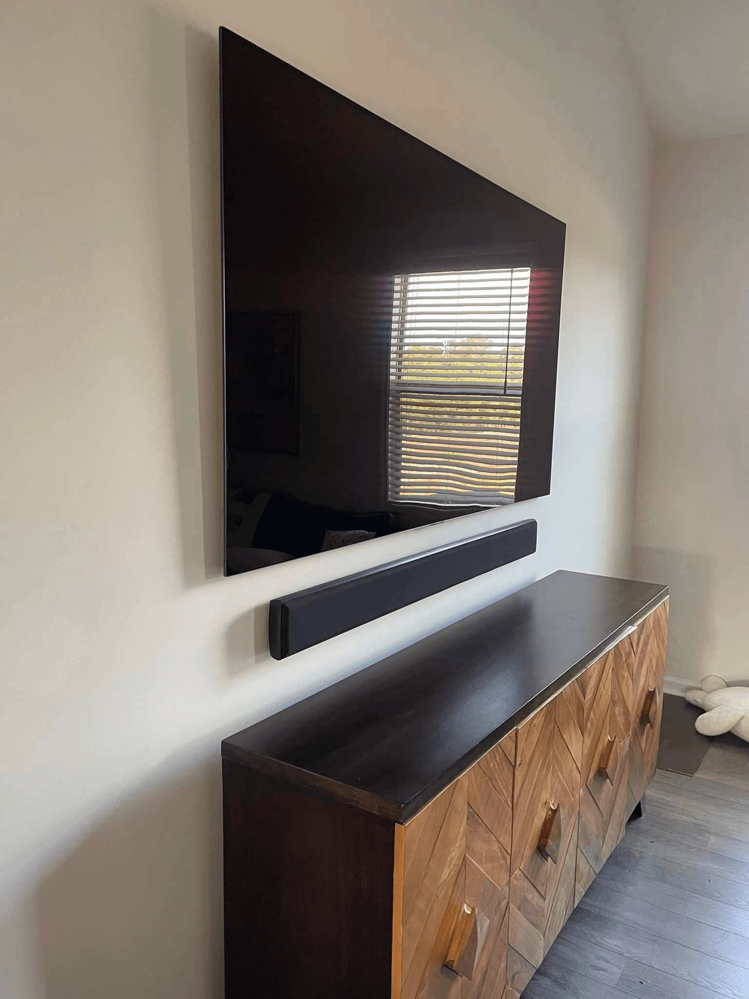 TV wall-mounted with soundbar above geometric wood credenza in bedroom
