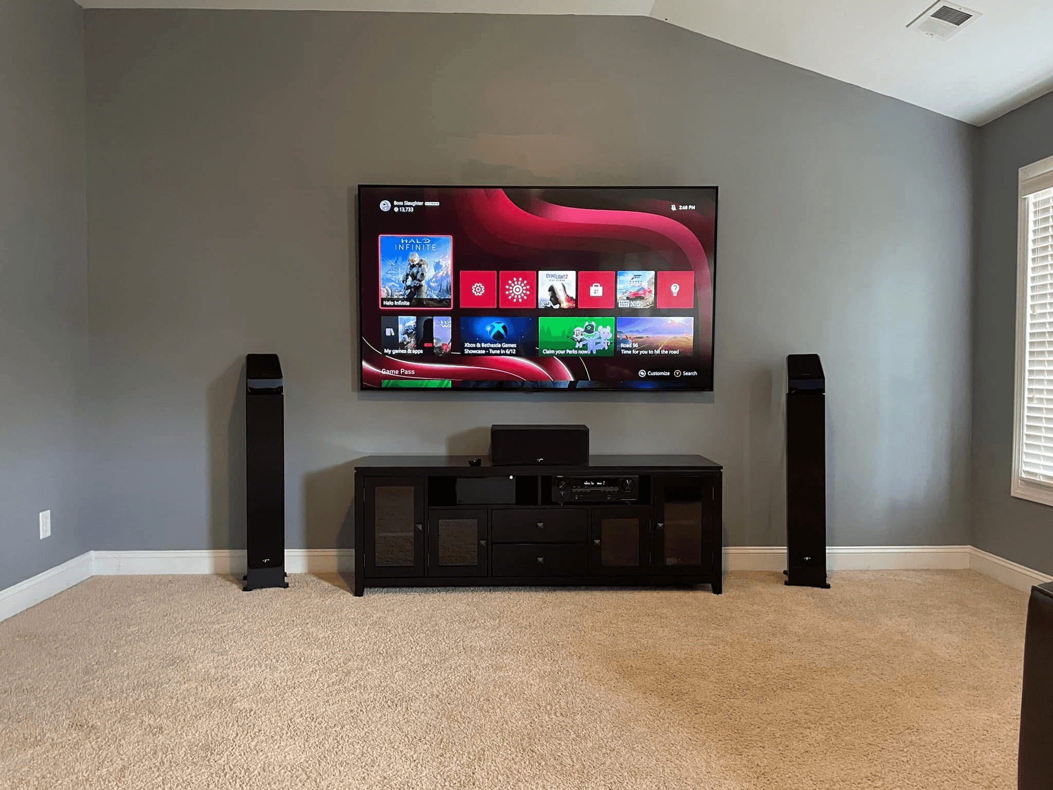 Large TV on gray wall with floor-standing tower speakers and AV receiver setup
