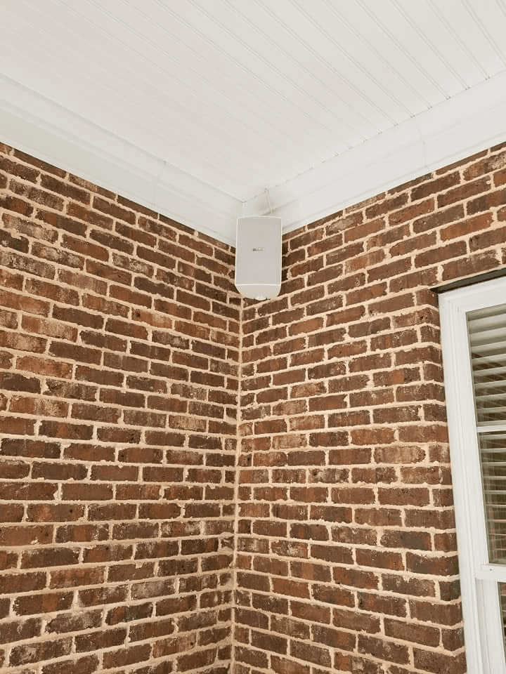 Wall-mounted outdoor speaker in brick corner of covered porch