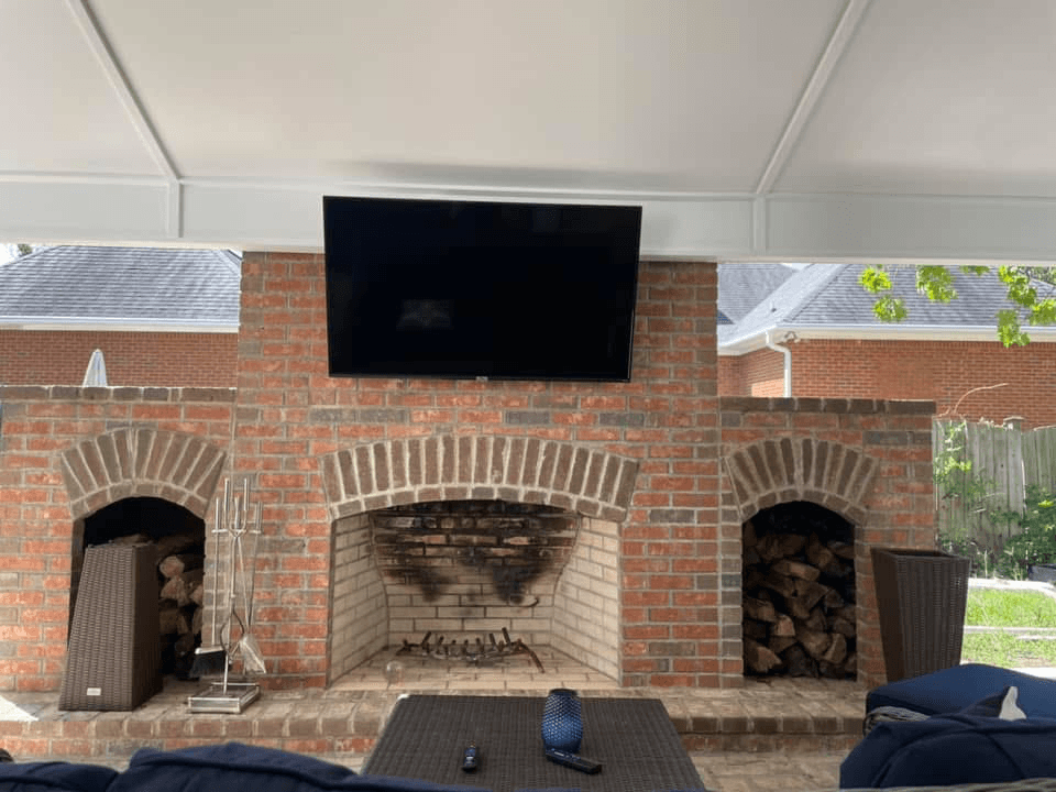 TV mounted above outdoor brick fireplace with firewood storage