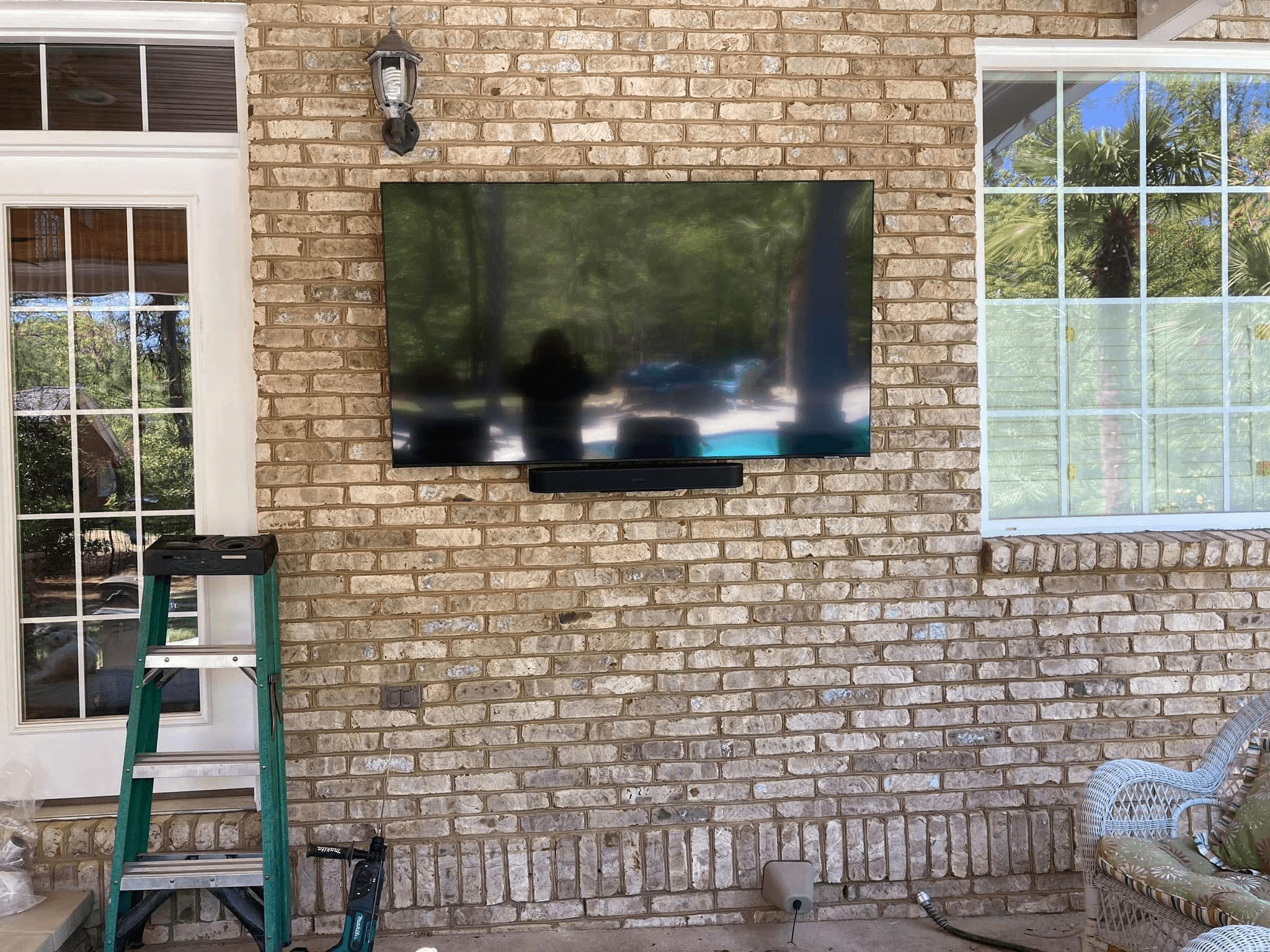 TV mounted on exterior brick patio wall with ladder during installation