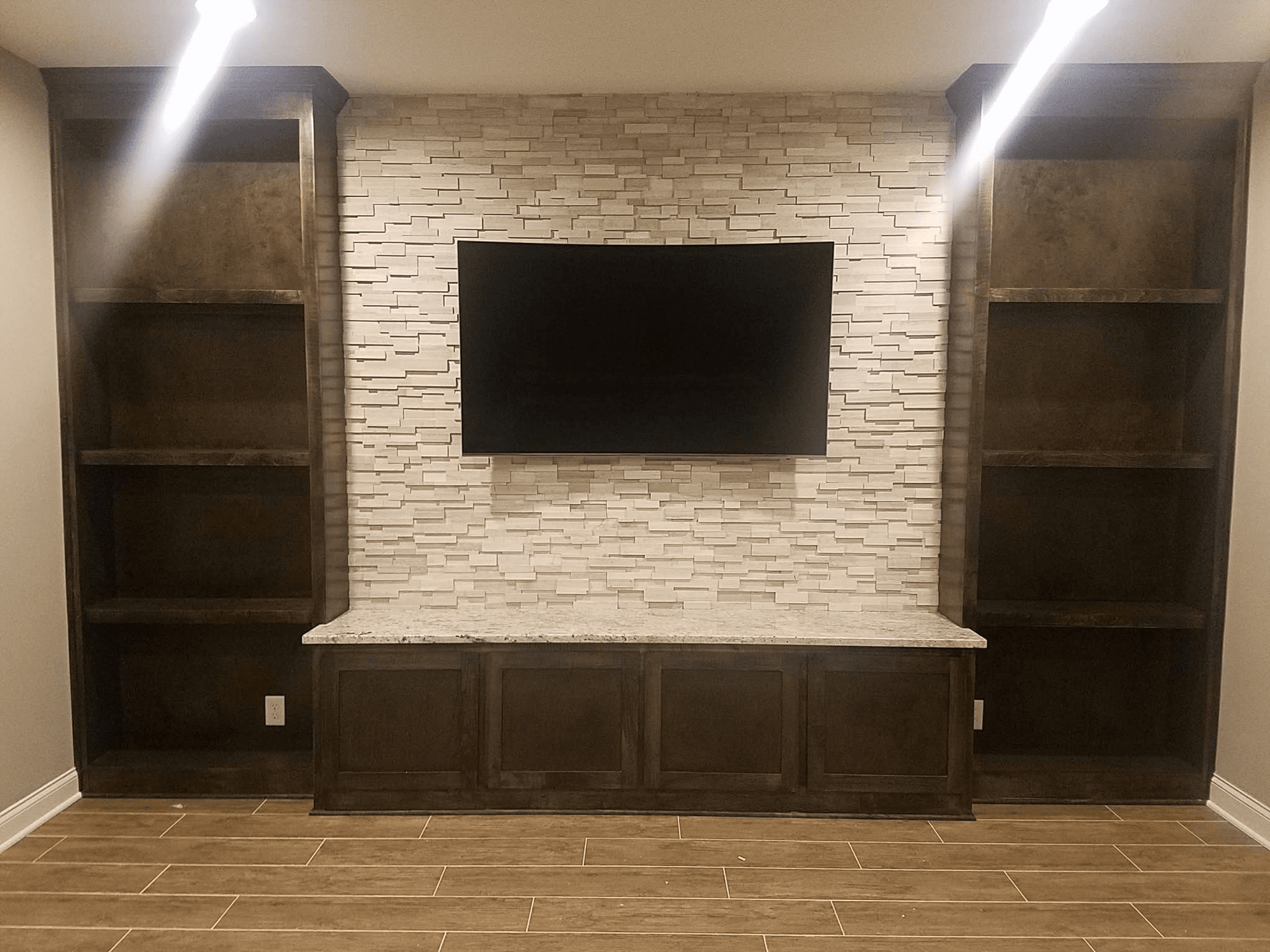 TV flush-mounted on white stacked stone entertainment wall with dark built-in cabinets