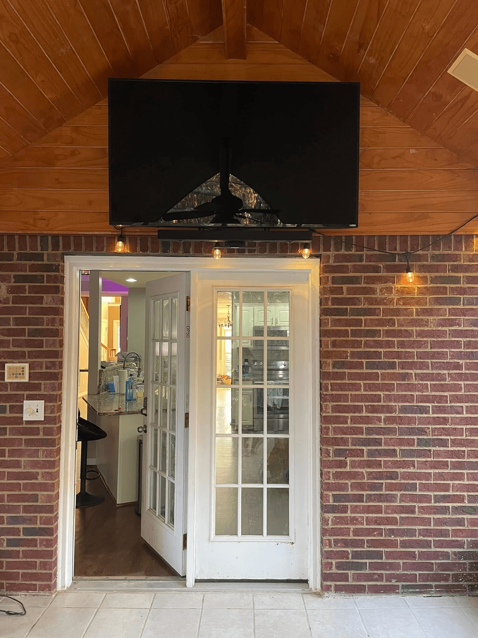 TV mounted high on vaulted wood ceiling above brick wall and french doors