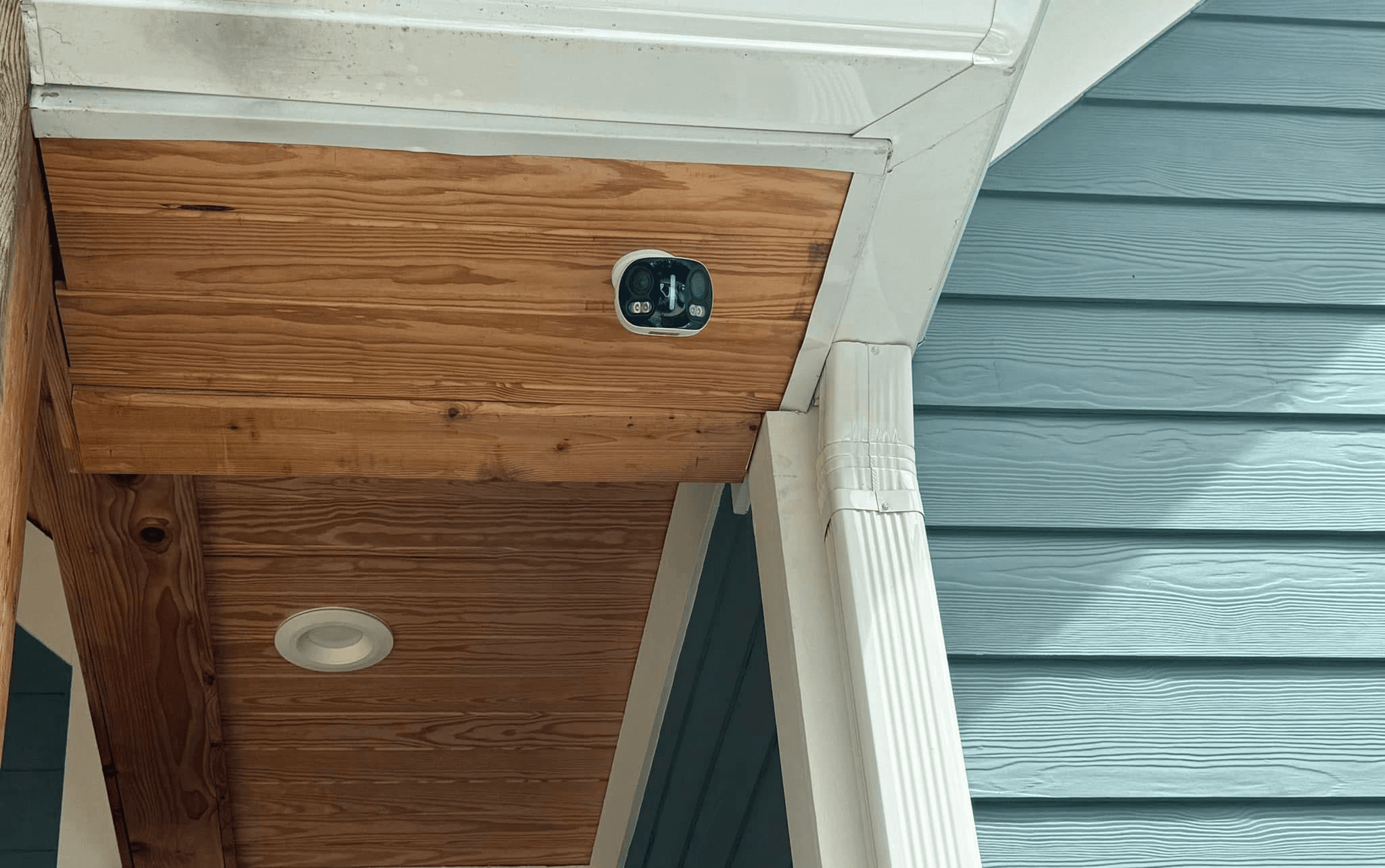 Security camera mounted under porch soffit on wood ceiling