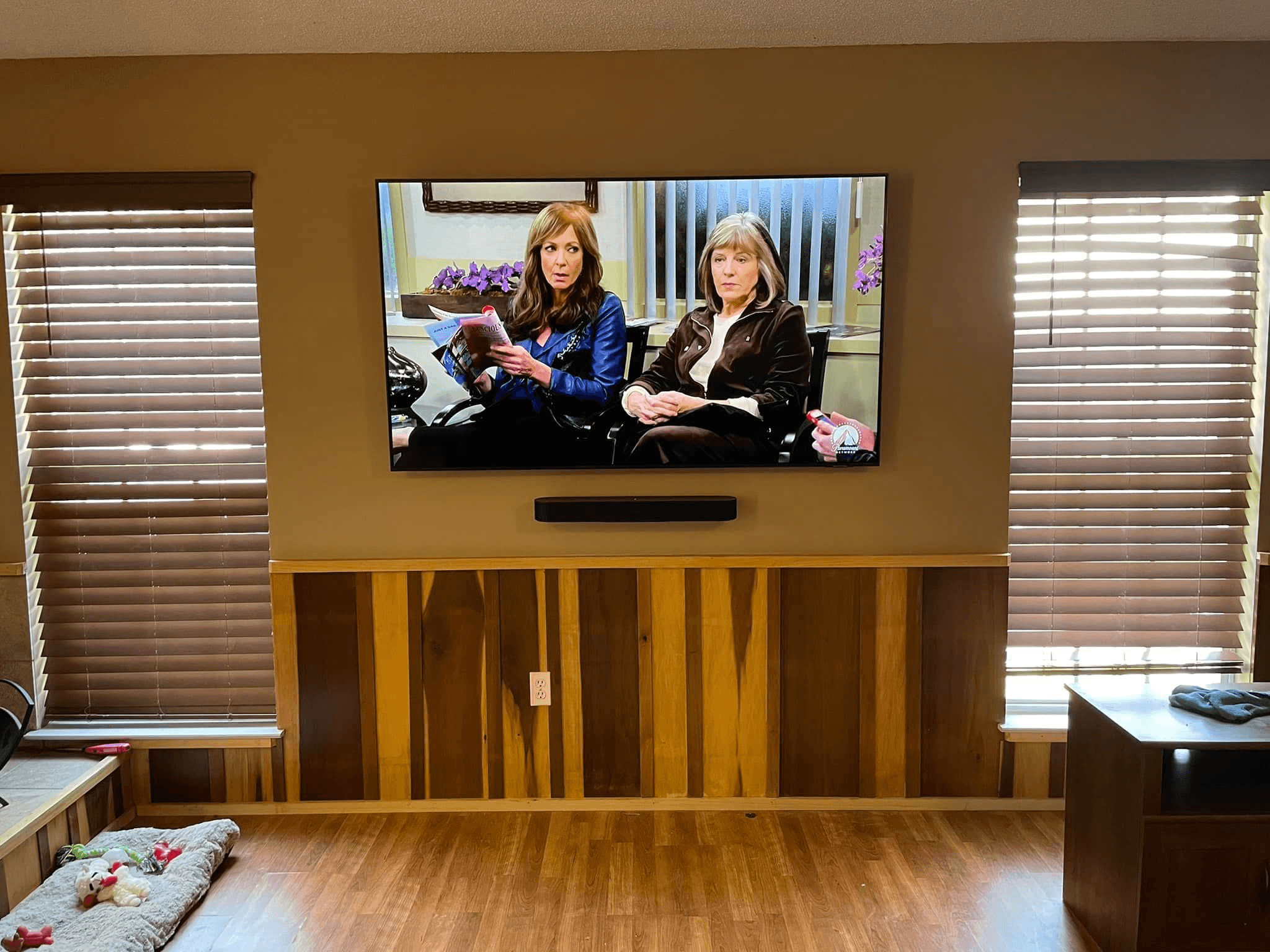 TV with Sonos soundbar mounted between windows above wood paneling in den